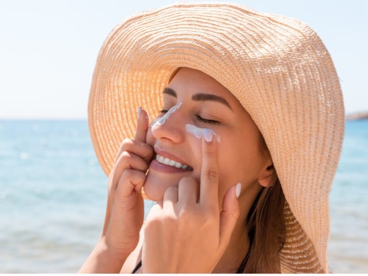 proteção solar para pele oleosa, mulher passando protetor no rosto na praia